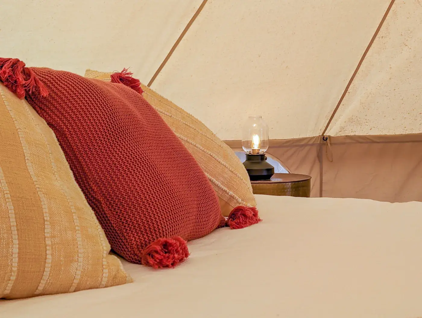 Cushions on the bed with a lantern lit on the side table