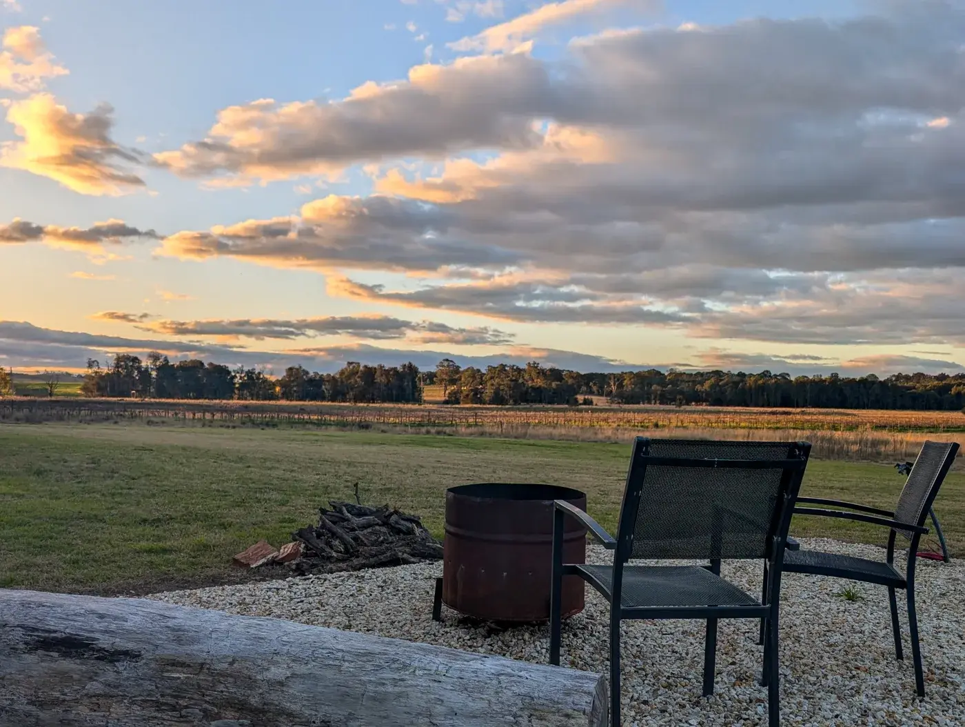 Two chairs beside the firepit, cut wood waiting, sunset over the paddocks