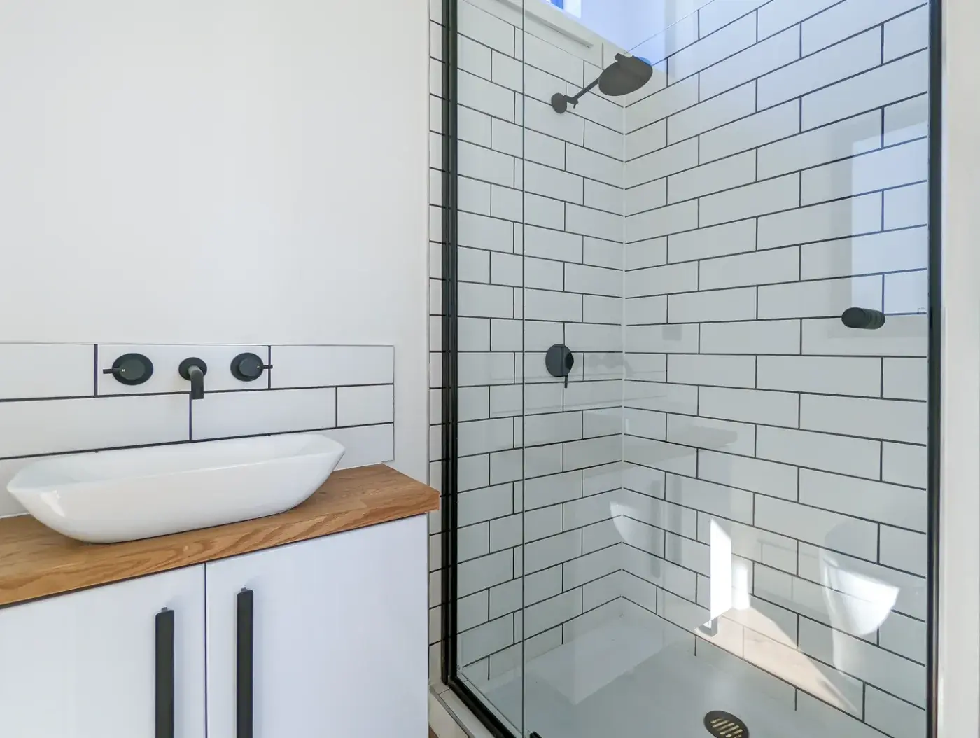 The pod bathroom, tiled shower and a basin on a timber bench