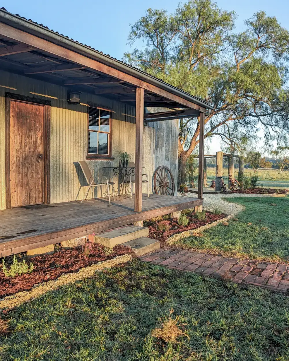 Early morning sun along the Cottage verandah, table and chairs on the deck and the paddocks beyond
