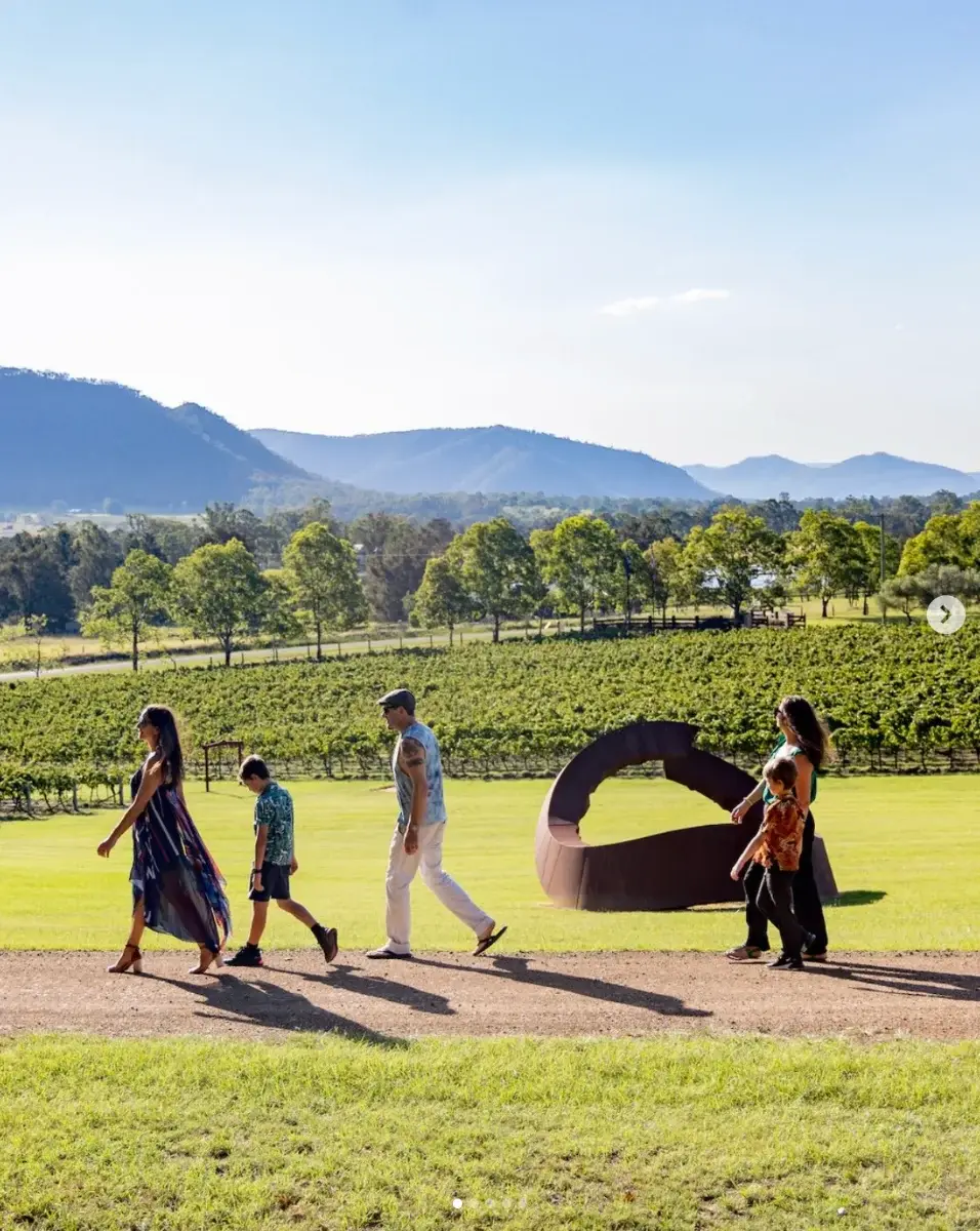A family walking past a sculpture on the lawn at Winmark, with vines and the Brokenback Range behind
